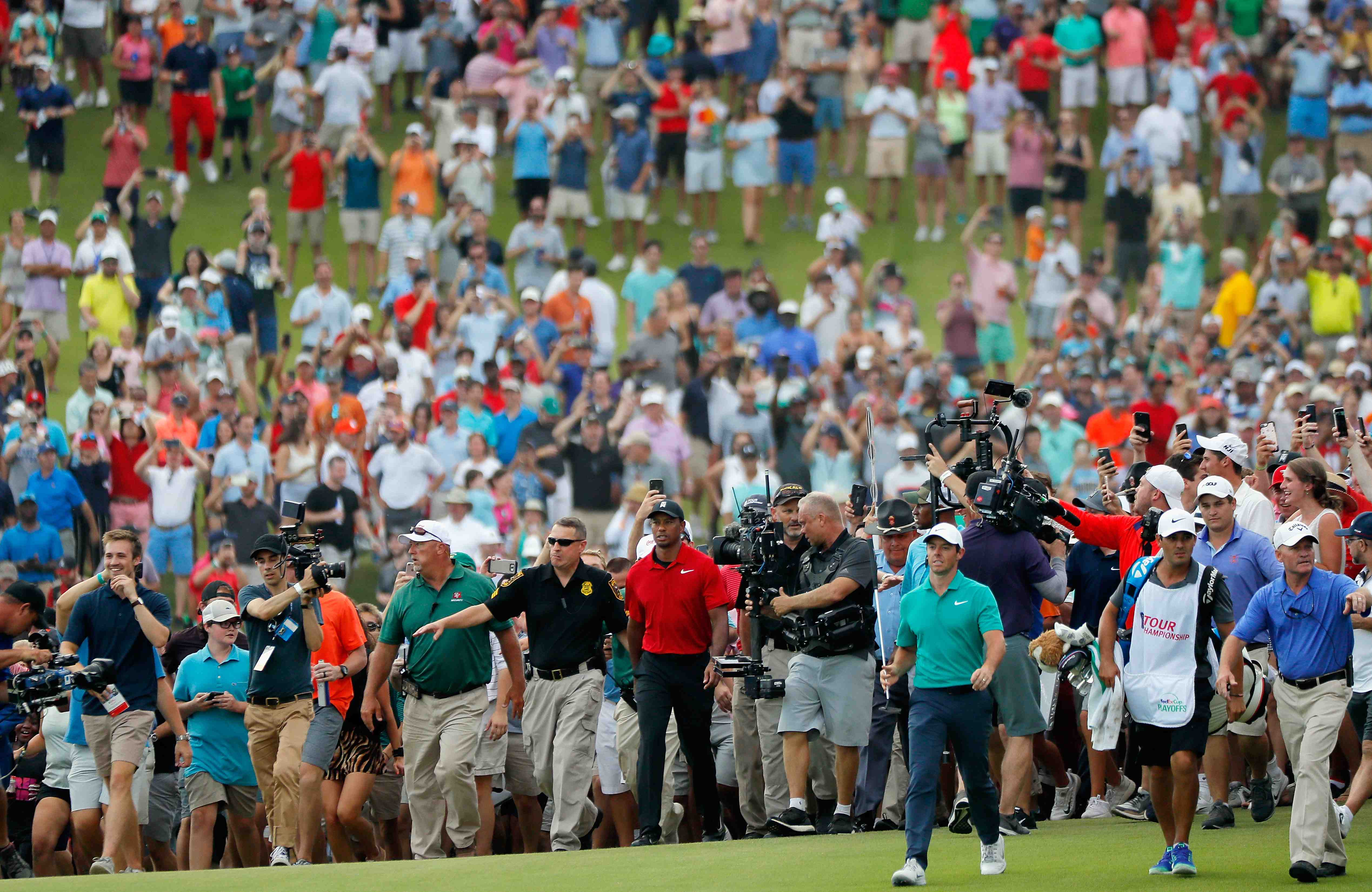 Tiger Woods y Rory Macilroy caminan con una orda de aficionados detrás suyo.